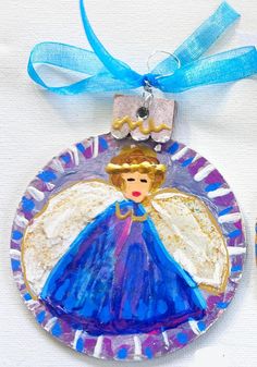 a glass ornament with an angel on it and a blue ribbon around the edge