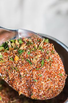 a spoon full of seasoning sitting on top of a pan filled with meat and vegetables