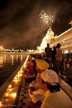 people sitting on the edge of a lake watching fireworks