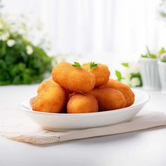 a white bowl filled with fried food sitting on top of a table next to green plants