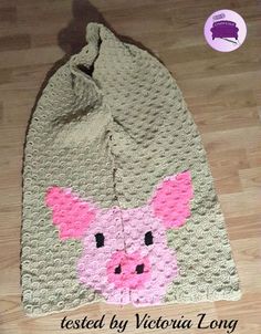 a crocheted bag with a pink pig on the front and bottom, sitting on top of a wooden floor