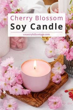 a pink candle sitting on top of a wooden tray next to some flowers and candles