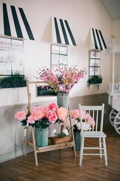 pink flowers are in buckets next to two white chairs