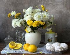 a white vase filled with yellow and white flowers next to lemons on a table