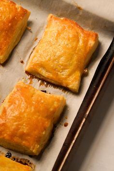 four square pastries sitting on top of a baking sheet next to a spatula