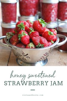 a bowl full of strawberries sitting on top of a table next to jam jars