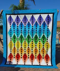 a colorful quilt hanging from the side of a palm tree