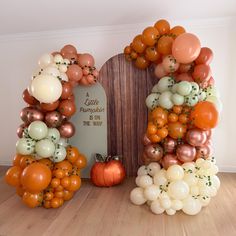 an arch made out of balloons and pumpkins sits on the floor next to a plaque