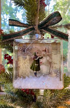 a glass ornament hanging from a christmas tree with snowman and girl on it