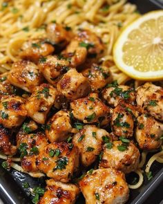 chicken and noodles with lemon wedges on the side in a black tray, ready to be eaten