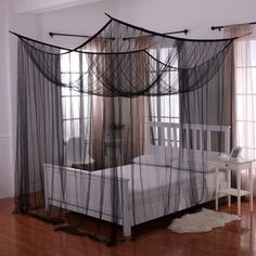 a white bed sitting on top of a hard wood floor next to a window covered in mosquito netting