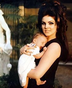 a woman holding a baby in her arms and looking at the camera while standing next to a statue