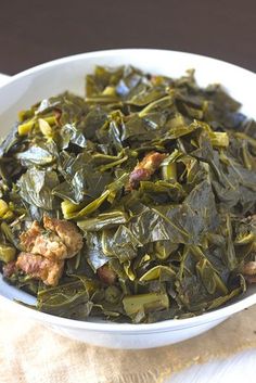 a white bowl filled with collard greens on top of a wooden table next to a napkin