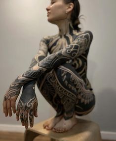 a woman sitting on top of a stool with tattoos on her arms and hands,