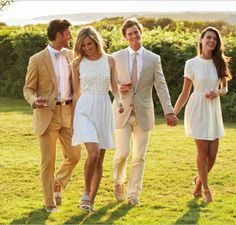 a group of people walking across a lush green field holding hands and wearing white dresses