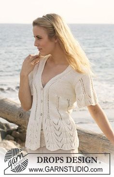 a woman standing on top of a beach next to the ocean wearing a white sweater