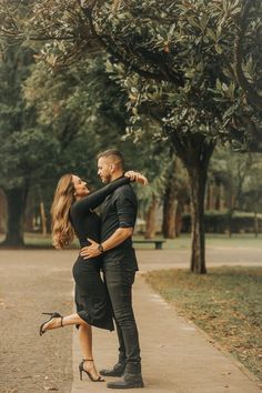 a man and woman embracing each other in front of trees with their arms around each other