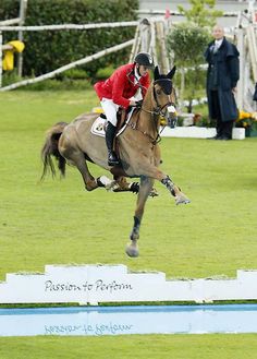 a man riding on the back of a brown horse while jumping over an obstacle in a field