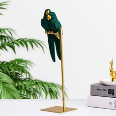 a green parrot sitting on top of a metal pole next to a book and plant