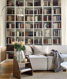 a living room with bookshelves full of books and flowers in vases on the coffee table