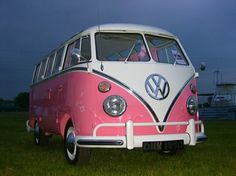 a pink and white vw bus parked on top of a grass covered field at night