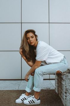 a woman in white shirt and jeans posing for a photo with her hands on her knees