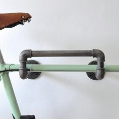 a green bike is hanging on a white wall and has two bars attached to the handlebars