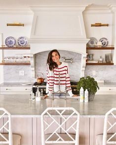 a woman standing in the middle of a kitchen with white cabinets and marble counter tops