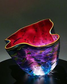 a colorful glass bowl sitting on top of a black table next to a white wall