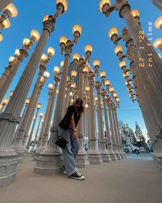 a woman taking a selfie in front of many lit up columns and lamps at dusk