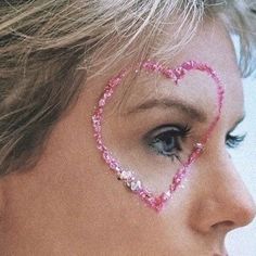 a close up of a woman with pink eyeliners and a heart drawn on her face