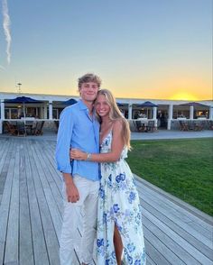 a man and woman posing for a photo on a wooden deck at sunset with the sun setting in the background