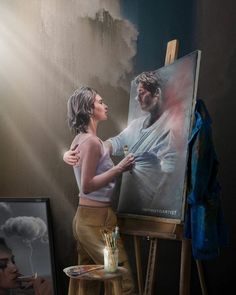 a woman standing in front of an easel painting a man's image on the canvas