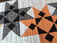 an orange and black star quilt on top of a wooden table