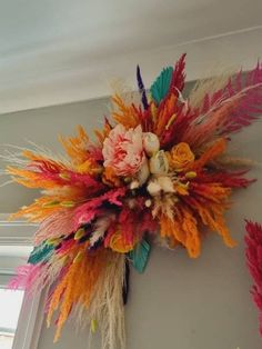 an arrangement of flowers and feathers hangs on the wall