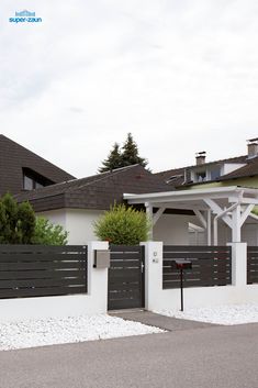 a white house with a black fence and some bushes on the side of the road