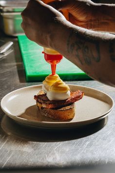 a person is pouring sauce on a bacon and egg sandwich