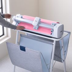 a woman is using a pink and white machine to print something on a sheet of paper