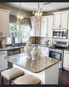 a kitchen with white cabinets and granite counter tops, two stools at the island