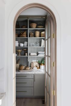 an open door leading into a kitchen with gray cabinets and white counter tops, along with baskets on the shelves