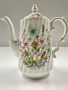 a teapot with flowers painted on it sitting on a white counter top next to a wall