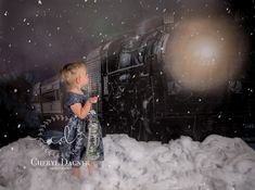 a little boy standing in the snow next to a train