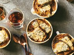 four bowls filled with food sitting on top of a table next to glasses and spoons