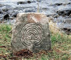 a stone sitting in the grass next to a river with a spiral design on it