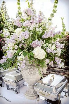 a vase filled with lots of flowers sitting on top of a table next to silver containers