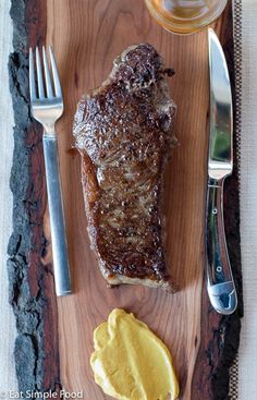 a piece of steak on a wooden cutting board with butter and fork next to it