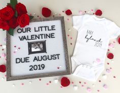 two baby onesuits with red roses on them and a sign that says our little valentine due august 2019