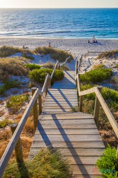 a wooden walkway leading to the beach with people in the water and sand dunes behind it