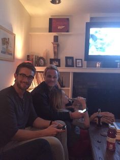 three people sitting on couches in front of a flat screen tv with the television on