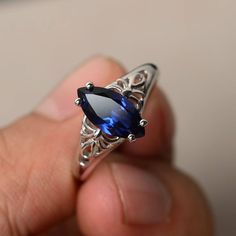 a hand holding a ring with a blue stone in it's center and filigrees on the sides